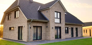 Krüppelwalmdachhaus mit Kapitänsgiebel und lehmgrauen Klinker mit anthraziten Fenstern auf grüner Rasenfläche